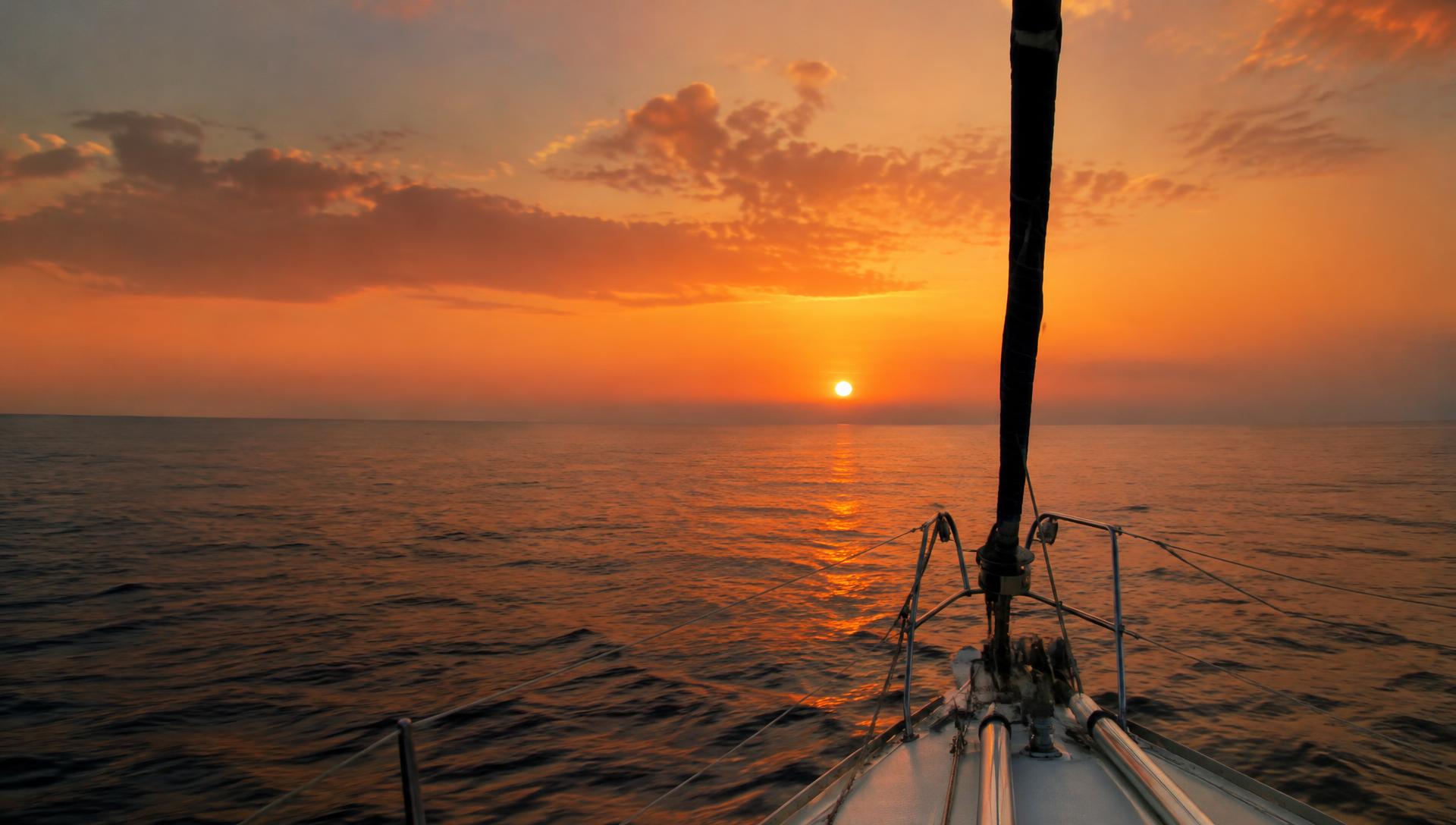 Sunset over the open sea from the bow of a sailing yacht